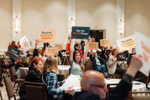 Attendees of the Chicago Bring No-Kill Home Summit smiling and holding up signs that say "Support TNVR", "Become a Network Neighbor", etc.